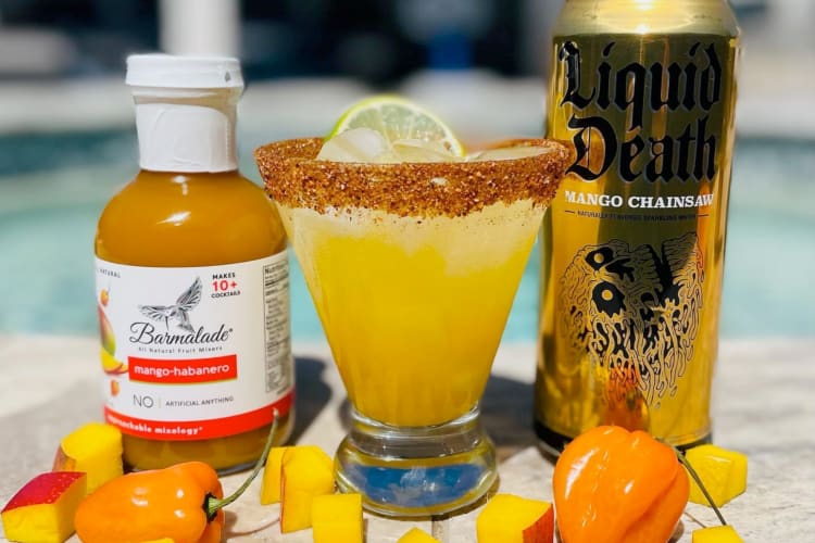A cocktail, mango and chile peppers next to a can of Liquid Death