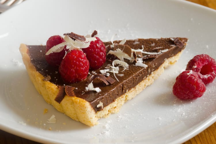 Slice of chocolate tart with raspberries and icing sugar on top