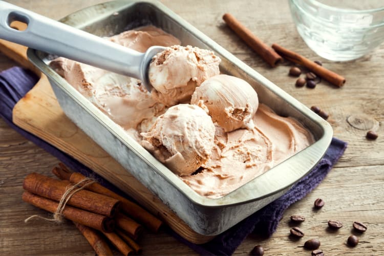A tub of scooped ice cream next to cinnamon sticks