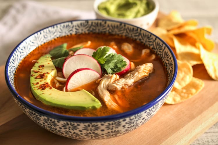 A bowl of pozole with avocado and radish