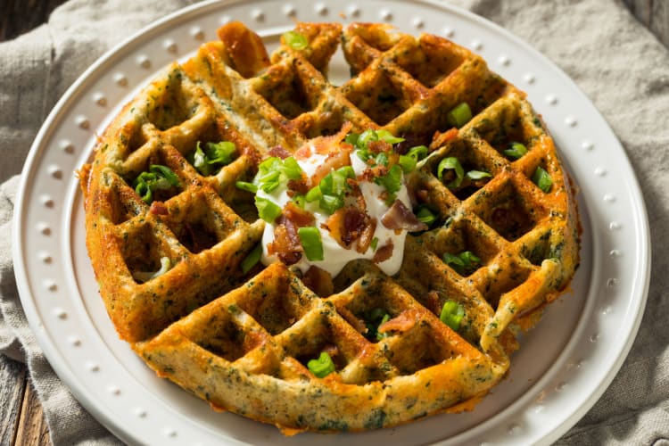 A savory waffle topped with sour cream, bacon and green onions