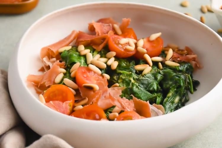 A salad with wilted spinach, pine nuts, tomatoes and Parma ham