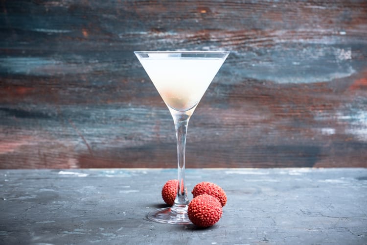 Eye-level view of a lychee vartini, a vodka cocktail, surrounded by lychees