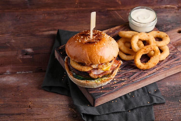Burger, onion rings and sauce on a wooden board