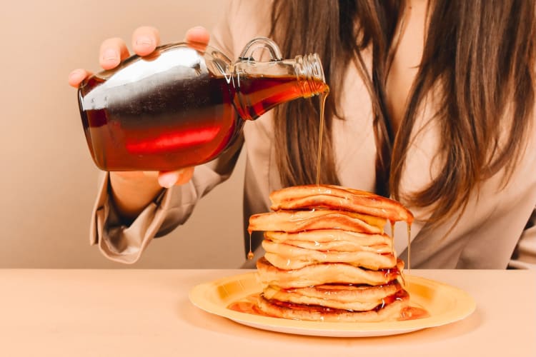 A person pouring syrup on pancakes