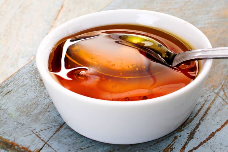 A white ceramic bowl with thick syrup and a spoon