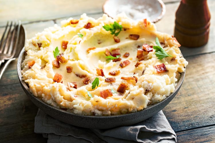 Bowl of mashed potatoes topped with bacon bits and fresh parsley
