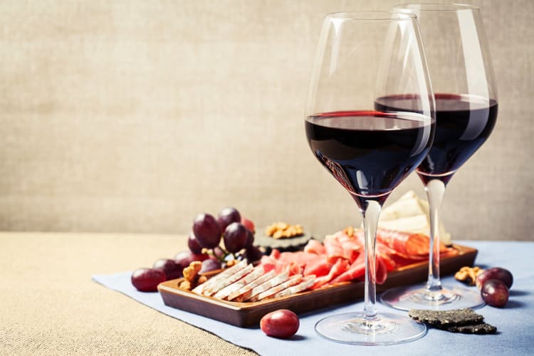 Two glasses of red wine next to a cheese and meat board