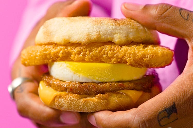 A person holding an English muffin with eggs, meat patty and has browns