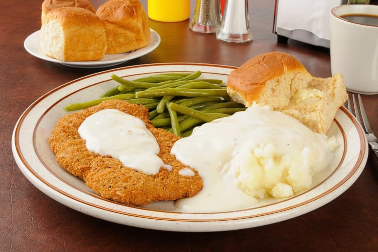 Chicken fried steak on a plate with green beans, mash and a roll