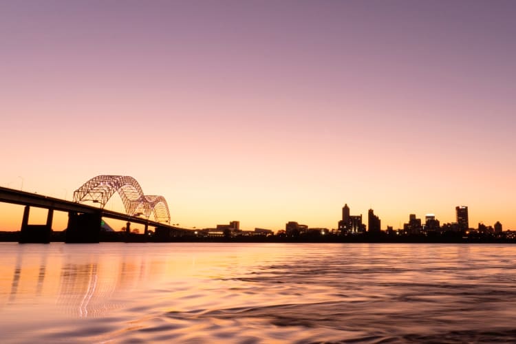 A bridge and city skyline next to the water at sunset
