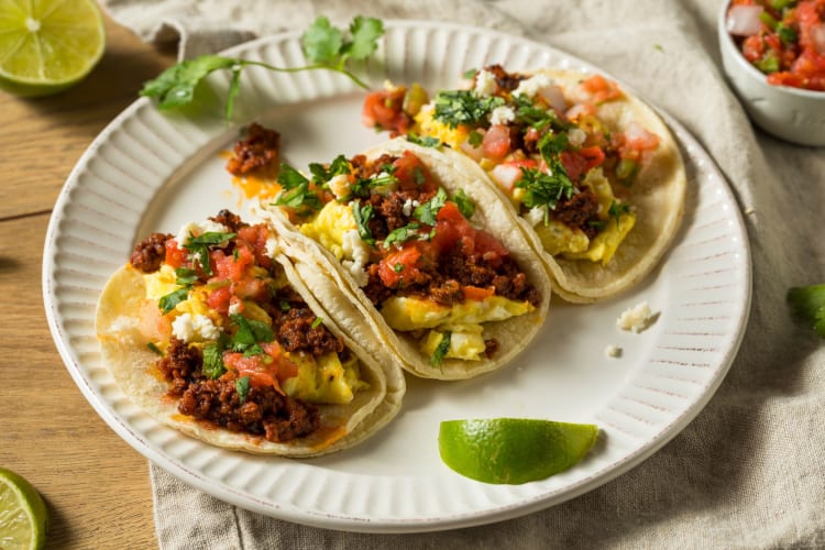 Three tacos on a plate with a lime wedge.