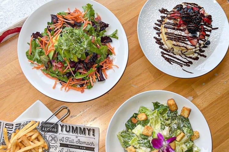 An overhead shot of plated salads and pancakes on a table