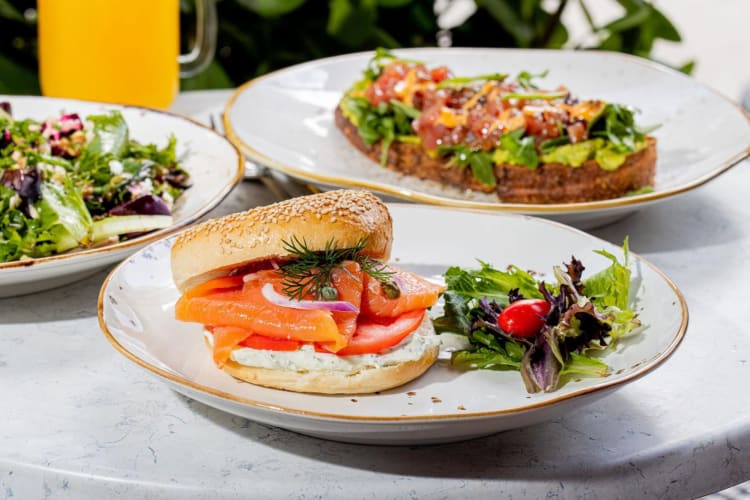 A bagel and lox on a plate on a table with other dishes behind it