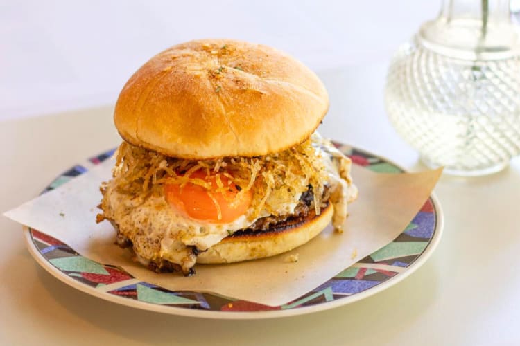 A breakfast sandwhich on a patterned plate with a glass vase behind