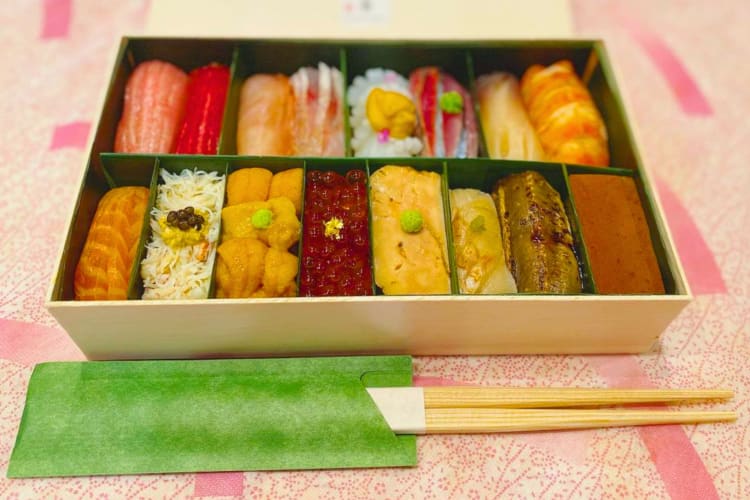 A box of nigiri next to chopsticks