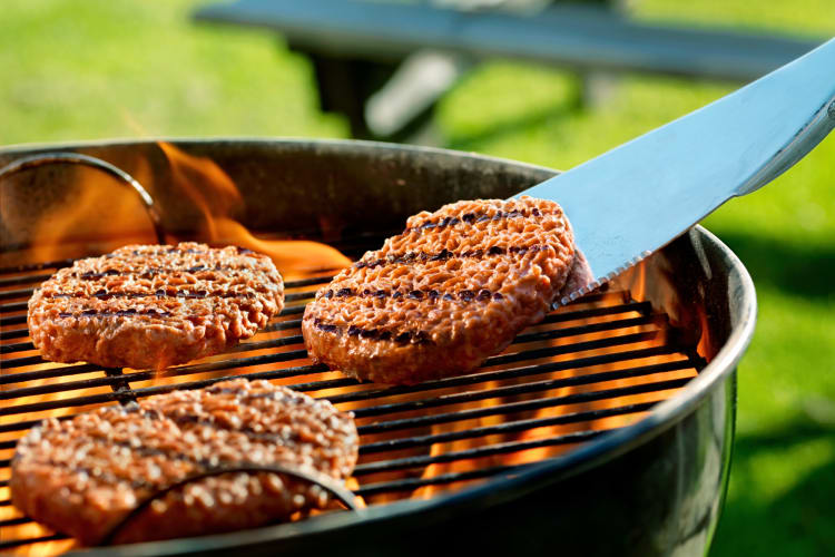 Three patties on a grill, one being flipped with a steel spatula