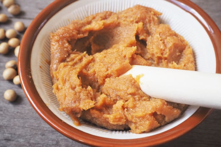 A ceramic bowl of miso paste next to soybeans