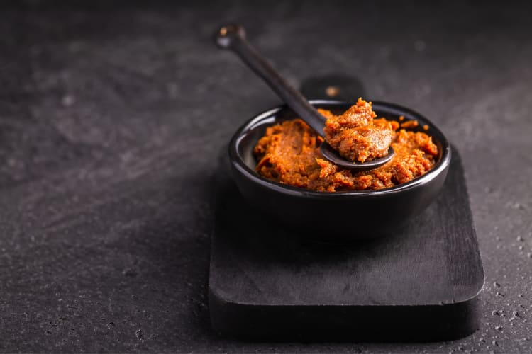 A bowl of red miso paste on a board with a spoon