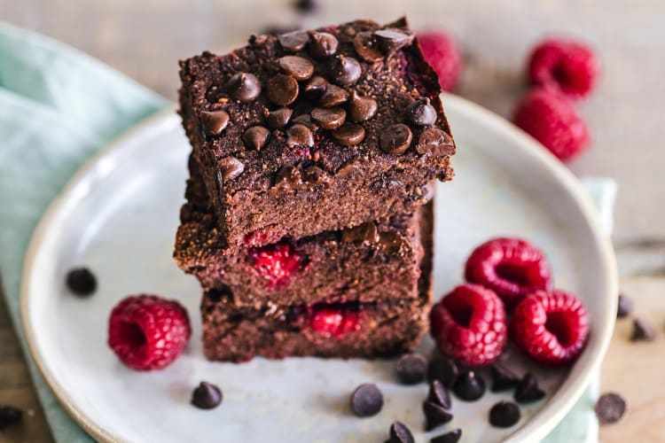 Three brownies in a stack surrounded by chocolate chips and raspberries