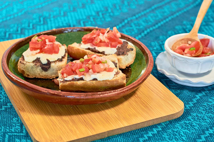 Three servings of mollete tostada on a plate next to a bowl of cut peppers