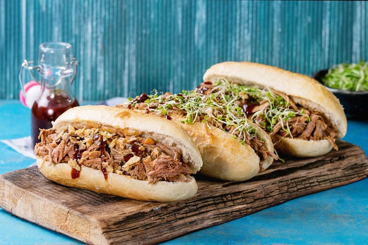 Three portions of montadito de pringá on a wooden serving board