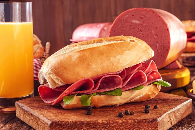 Mortadella sandwich in front of a glass of orange juice and mortadella portions