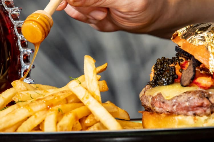 A burger with caviar next to fries drizzled with honey