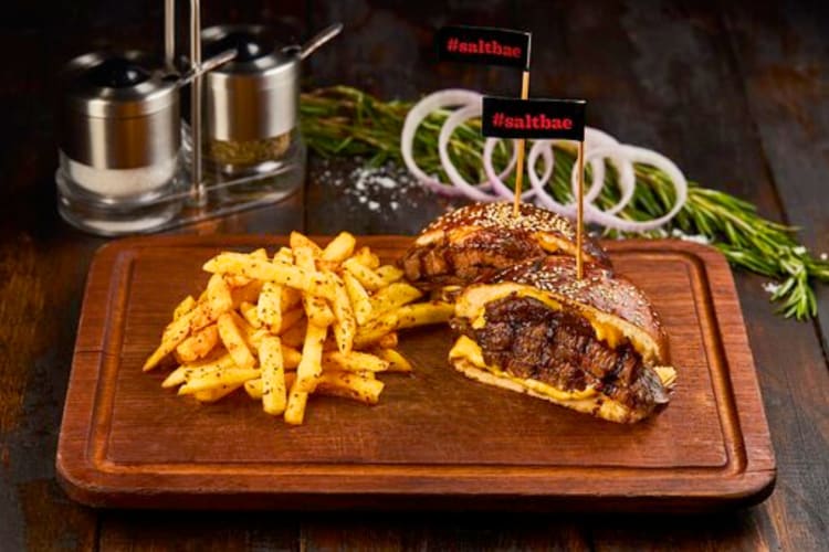 A burger cut in half next to fries on a wooden board