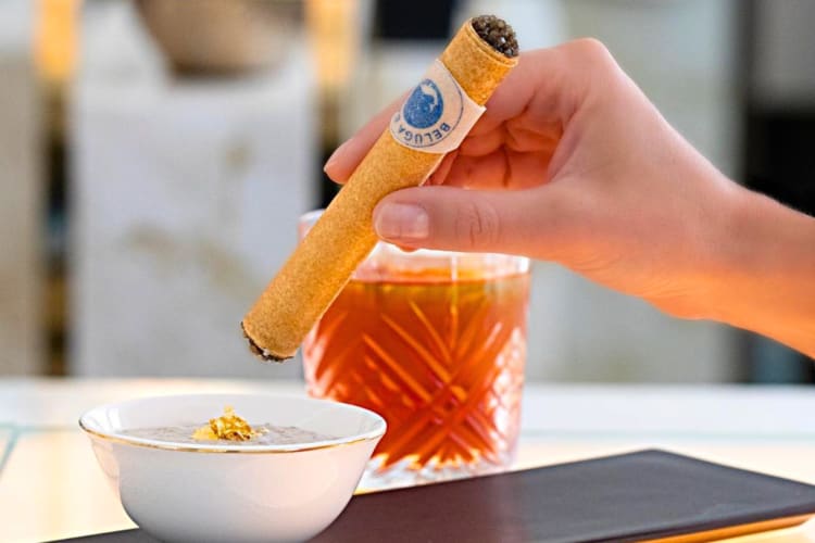 A women at a bar holding a golden cigar with caviar