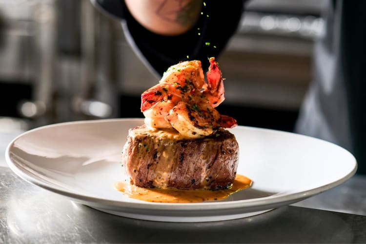 A steak with lobster on a black plate