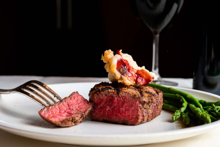 Steak and lobster on a plate with a glass of red wine in the background