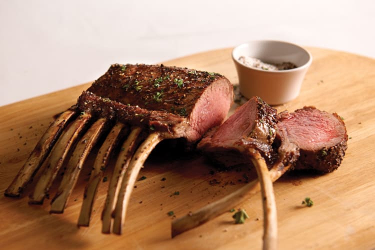 Lamb chops cooked to blushing pink on a wooden board with sauce.