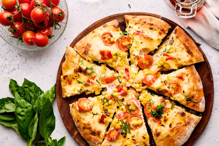 A pizza with lobster next to fresh basil and tomatoes