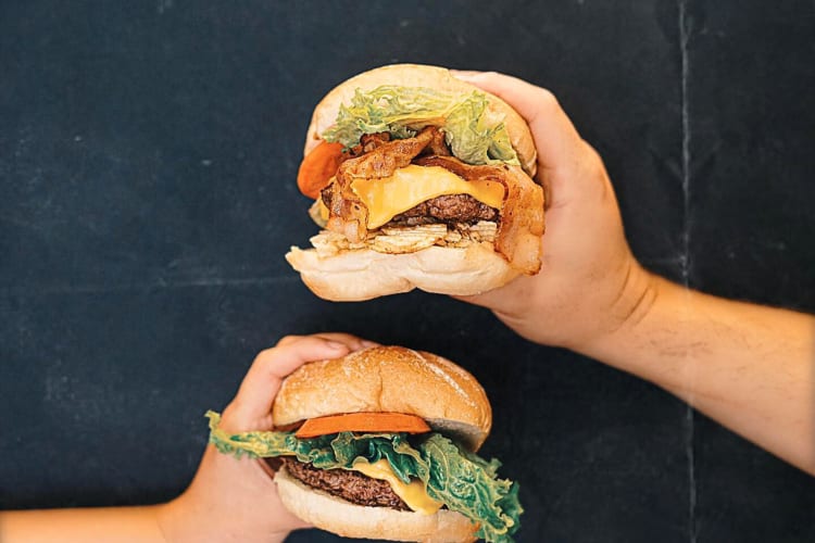 Two hands holding two burgers from Mr. Pepito Miami, a food truck in Miami