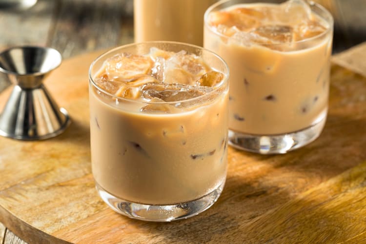 Two mudslide vodka cocktails on a wooden surface with a shot pourer
