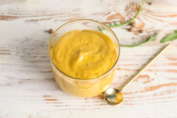 Mustard in a transparent bowl next to a spoon