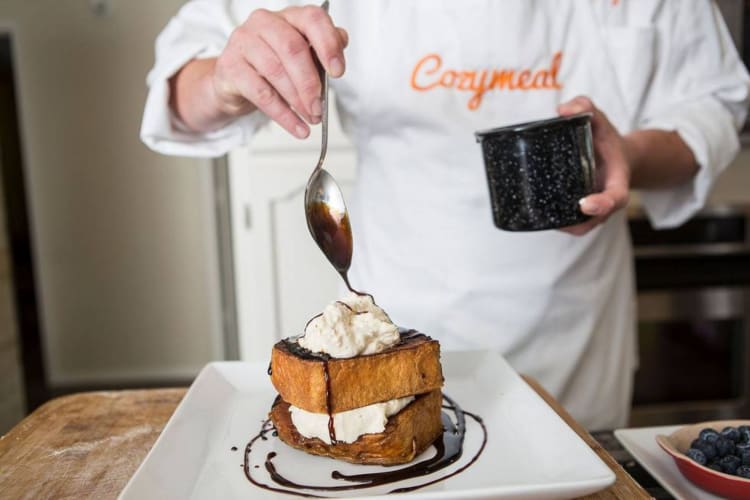 A chef in a Cozymeal apron pouring chocolate on French toast