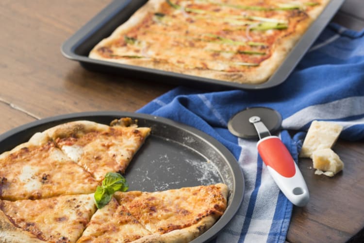 Two pizza pans with pizza next to a dish cloth