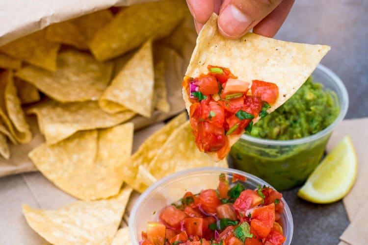 Close-up of a person's hand holding a nacho that's been dipped in salsa