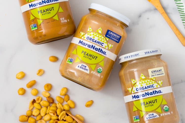 Three glass jars of peanut butter next to peanuts