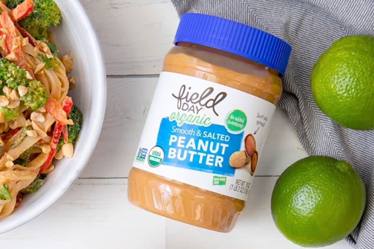A jar pf peanut butter next to a noodle bowl and fresh limes