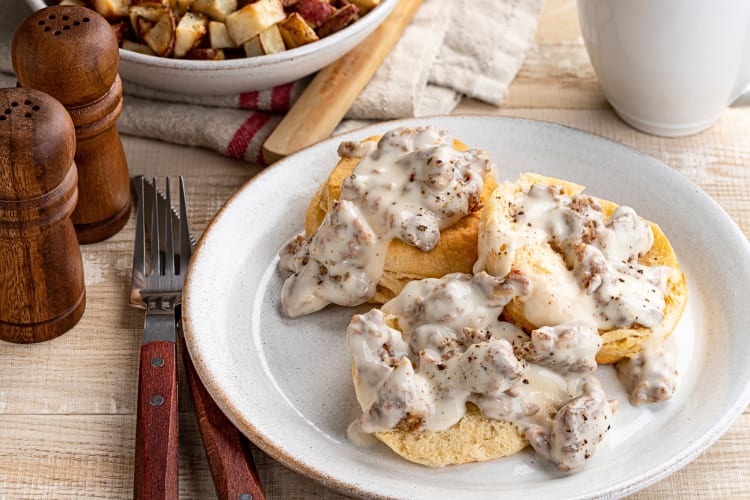 Biscuits and gravy next on a plate, next to a knife and fork, and salt and pepper shakers