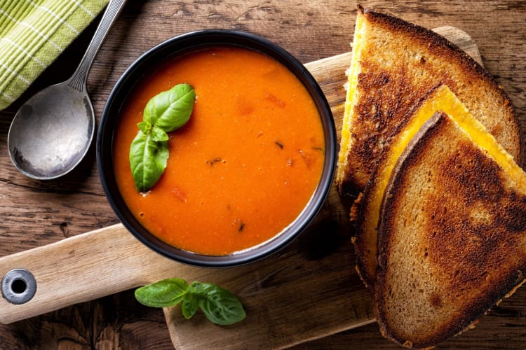 A bowl of tomato soup, garnished with basil with bread on the side.