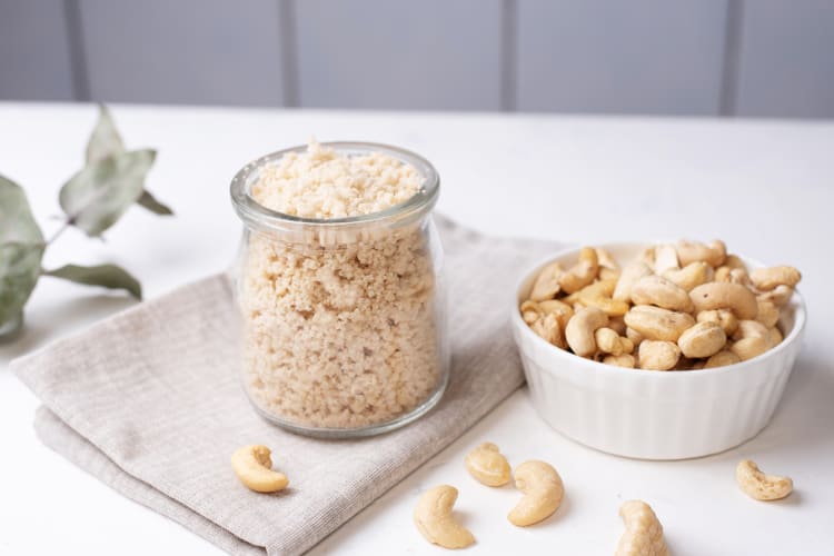 Cashews in a bowl next to a jar of crushed cashews