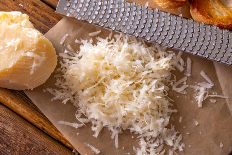 A block of parmesan next to grated cheese