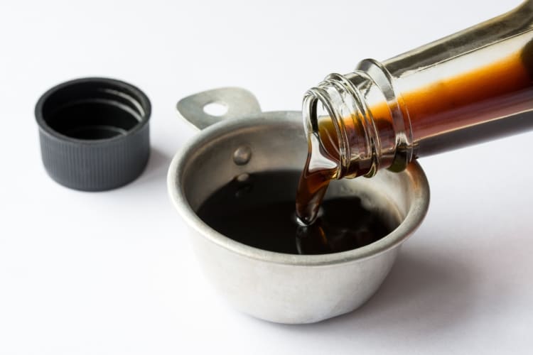 A brown liquid being poured from a bottle into a bowl