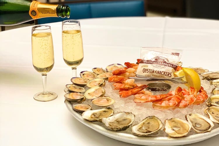 A platter of oysters next to two glasses of champagne, from Old Ebbitt Grill