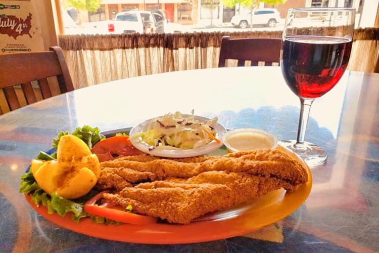 Chicken-fried steak meal with a side salad, next to a glass of wine, from Old Neighborhood Grill