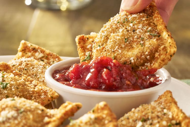 A person dipping a toasted ravioli into marinara sauce